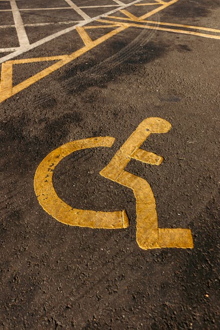 Close-up view of an empty parking space on an asphalt surface with clearly visible white painted lines and a circular symbol with the number '22' inside. The area appears to be part of a designated parking lot adjacent to a residential or commercial property. The surface is textured with small gravel and minor debris scattered around. The background shows additional parking spaces and a small section of the surrounding environment. This setting demonstrates typical parking lot markings relevant for vehicle loading or unloading during home relocation or furniture transport, as managed by firms such as Man with Van Newbury Park, which specialises in removals and moving services in the IG2 postcode area.